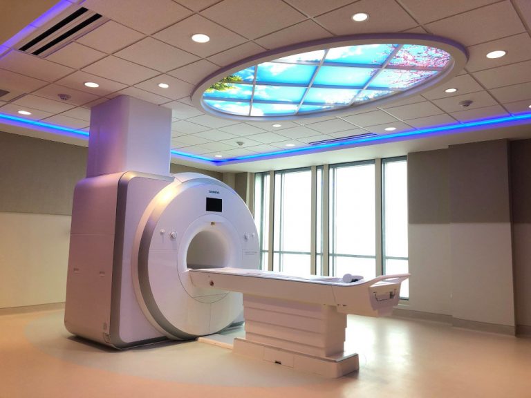Inside of the MRI treatment room at the Riverside Doctor's Hosptial showing their newest cylindrical MRI machine with a telescoping patient table both located under an oval skylight and accented by neon blue light.