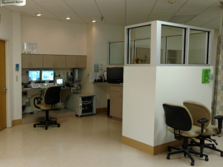 Full view of the raidiosurgery and xray control room including monitoring equipment and a lead shielded barrier wall with windows