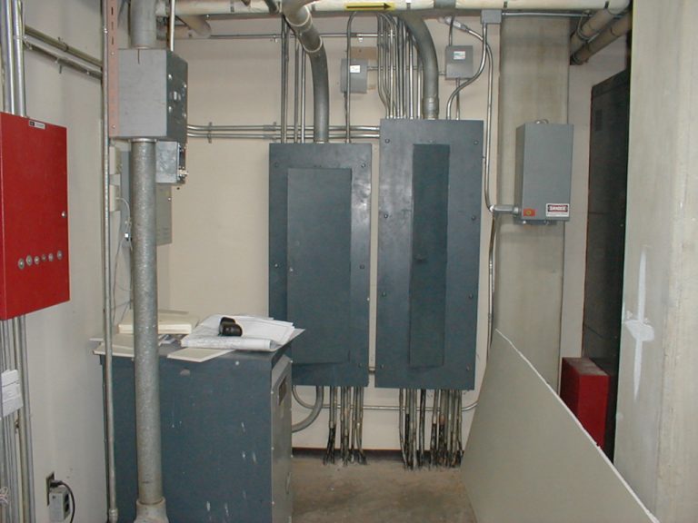Two large electrical distribution boards wall mounted in the mechanical room with a multitude of different sized conduits running into them