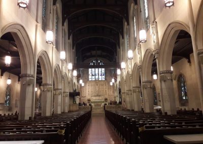 View of the sanctuary from the rear of the room showing all of the pews and classic arched walls with religious stoned carvings and stained glass behind the pulpit