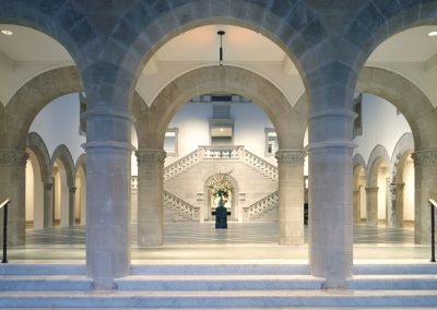 Wide marble stairs and multiple rows of marble columns and arches in front of a beautiful classic marble imperial staircase that make up an exhibition hall in the Chrysler Museum of Art