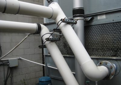Two large white pvc condenser water pipes diagonally mounted alongside hvac equipment and running parallel to each other