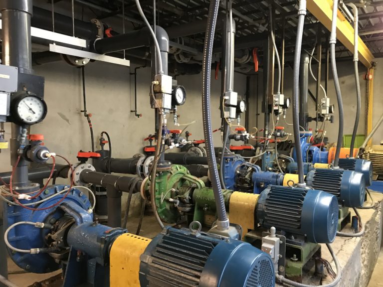 Five industrial size pumps all with pressure gauges and flanged piping connections in the pump house at the facility