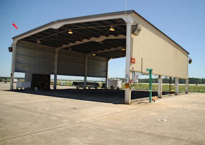 Extensive span of concrete pad with a giant metal open air Quonset hut type building containing ceiling mounted high-bay lighting at the airfield in Cherry Point North Carolina