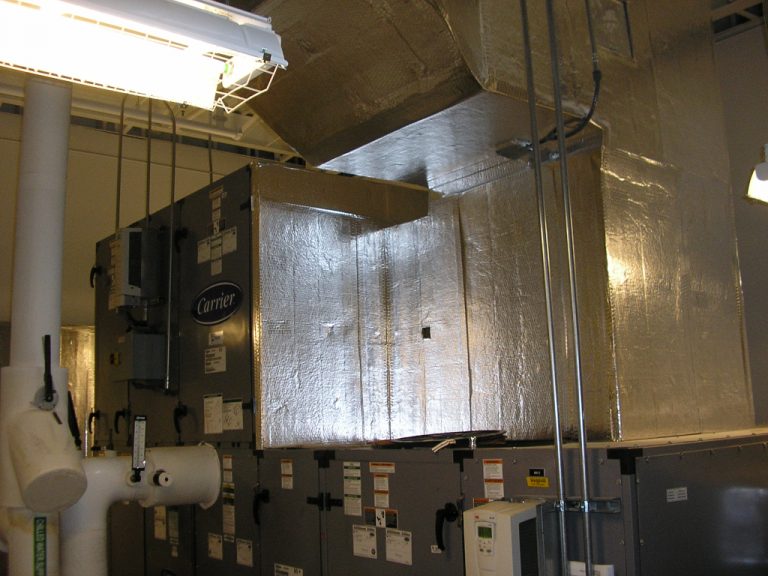 Large grey air handling unit with a silver flexible ductwork plenum attached to the top