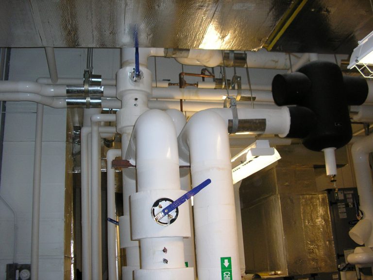 Various sizes of flow valves and vertical white pvc piping carrying chilled supply and return water to the building