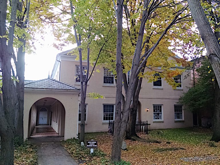 Leaf strewn lawn and trees in front of the entrance to the church offices and the colonnade leading to the sanctuary