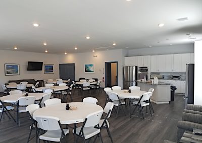 Meeting and dining room with multiple round tables and chairs next to a breakfast bar and full kitchen in the recreation building of the Arizona RV Park