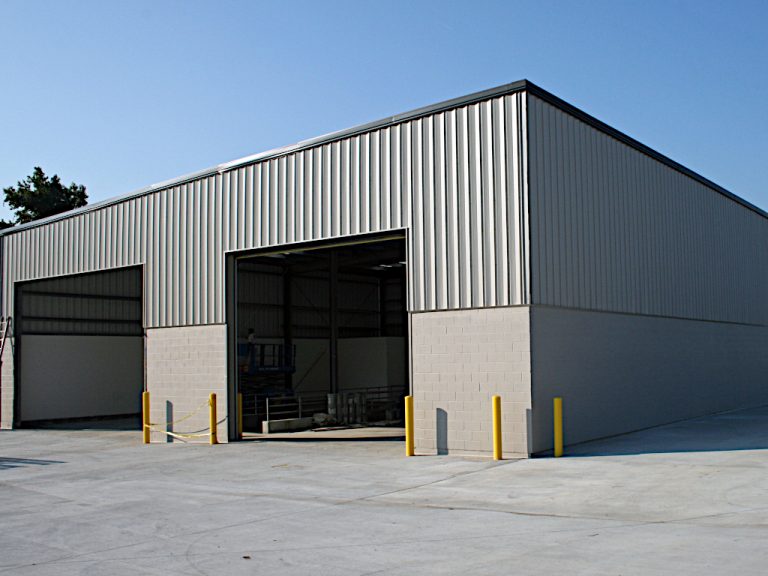 Exterior view of two open repair bay roll up doors in the gray metal and cinder block Carter Machinery building