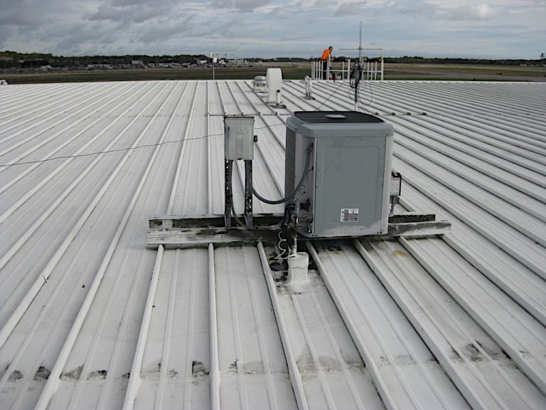 Large air handling unit and electrical breaker box mounted on a metal roof near an antennae and an exhaust fan