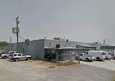 Dilapidated old building of the Epsilon System Warehouse with the main and side parking lots filled with white work vans and employee cars