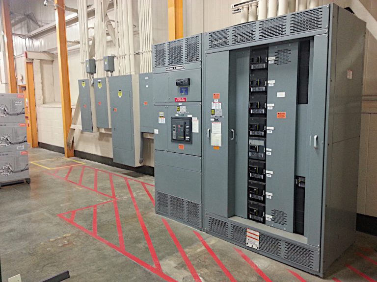 Industrial size transfer switch alongside emergency controls and four wall mounted electrical panels including conduits in the Stihl building mechanical room