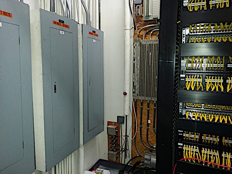 Wall mounted electrical panels and a metal rack full of cat 5 network connections in the utility room of the Stihl building