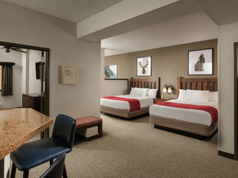 Interior view of a guest room with two hardwoood double beds and a marble breakfast bar with high-top chairs at Greatwolf Lodge Williamsburg