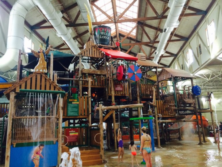 Adults and children playing in the giant wooden multi level fort type jungle gym with bridges and compartments adorned with lots of water activities