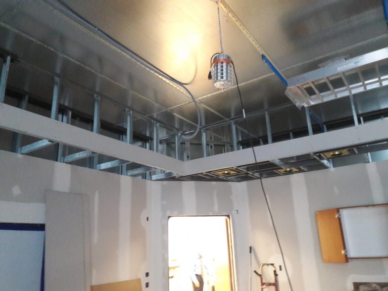 Unfinished construction of a treatment area showing partially plastered drywall and a bare metal frame for an interior soffit