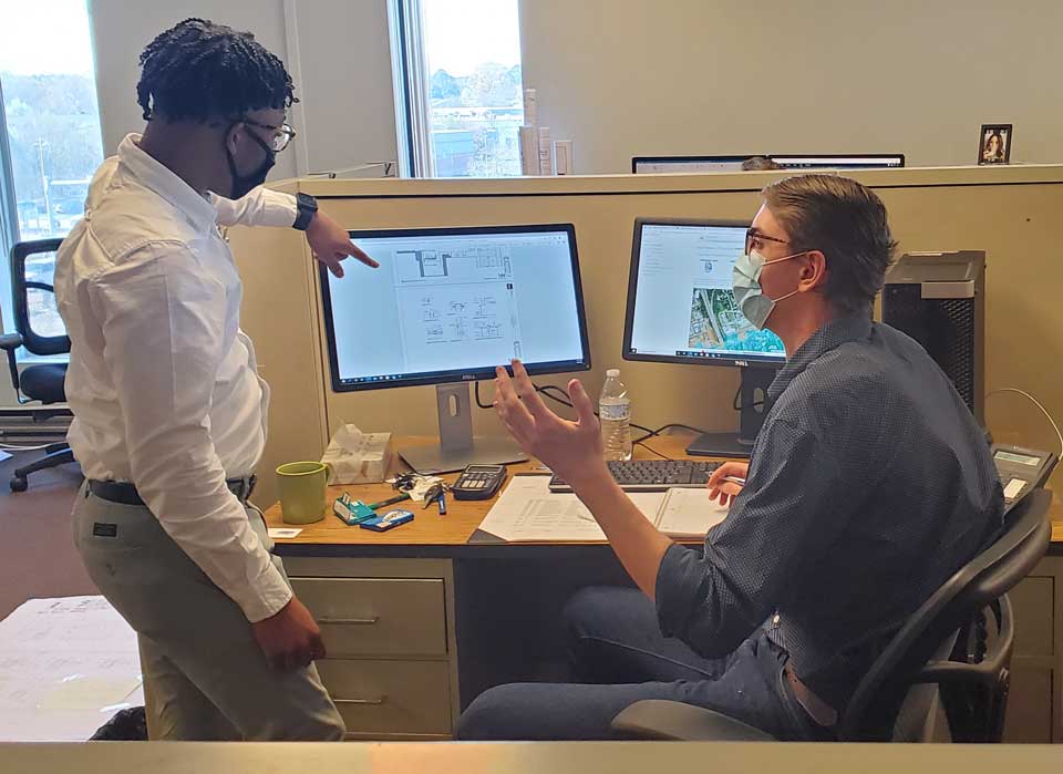 Two design professionals in front of a computer monitor pointing and discussing where plan changes occur