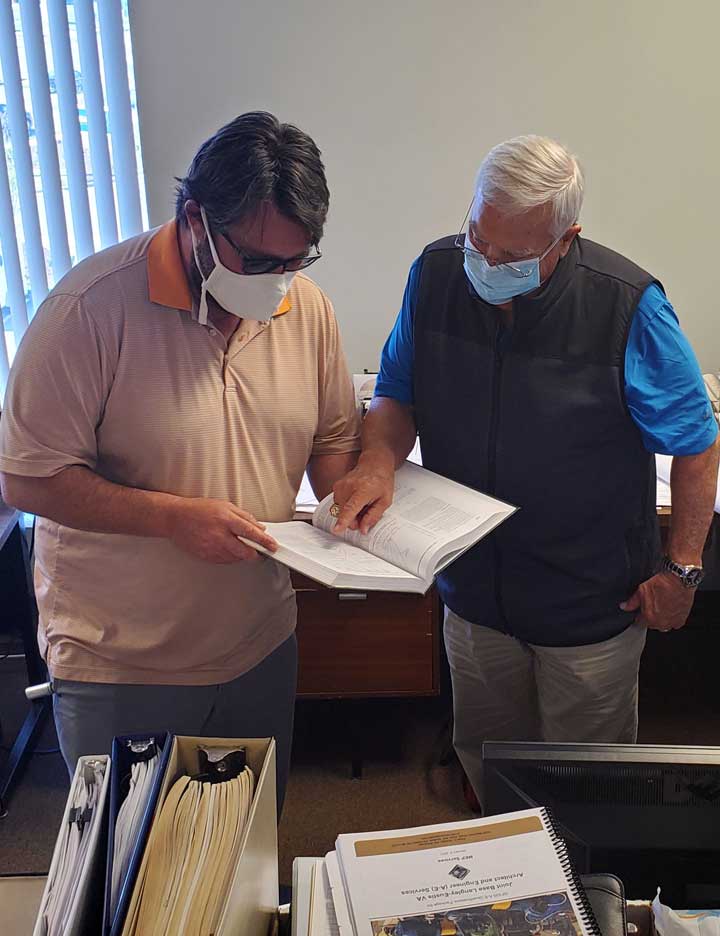 Two male engineers standing next to each other looking down in a book while researching information for proposal