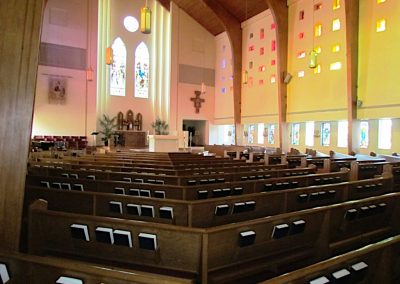 View of the sanctuary from the rear of the room showing all of the diagonally aligned pews and colorful walls and stained glass behind the pulpit