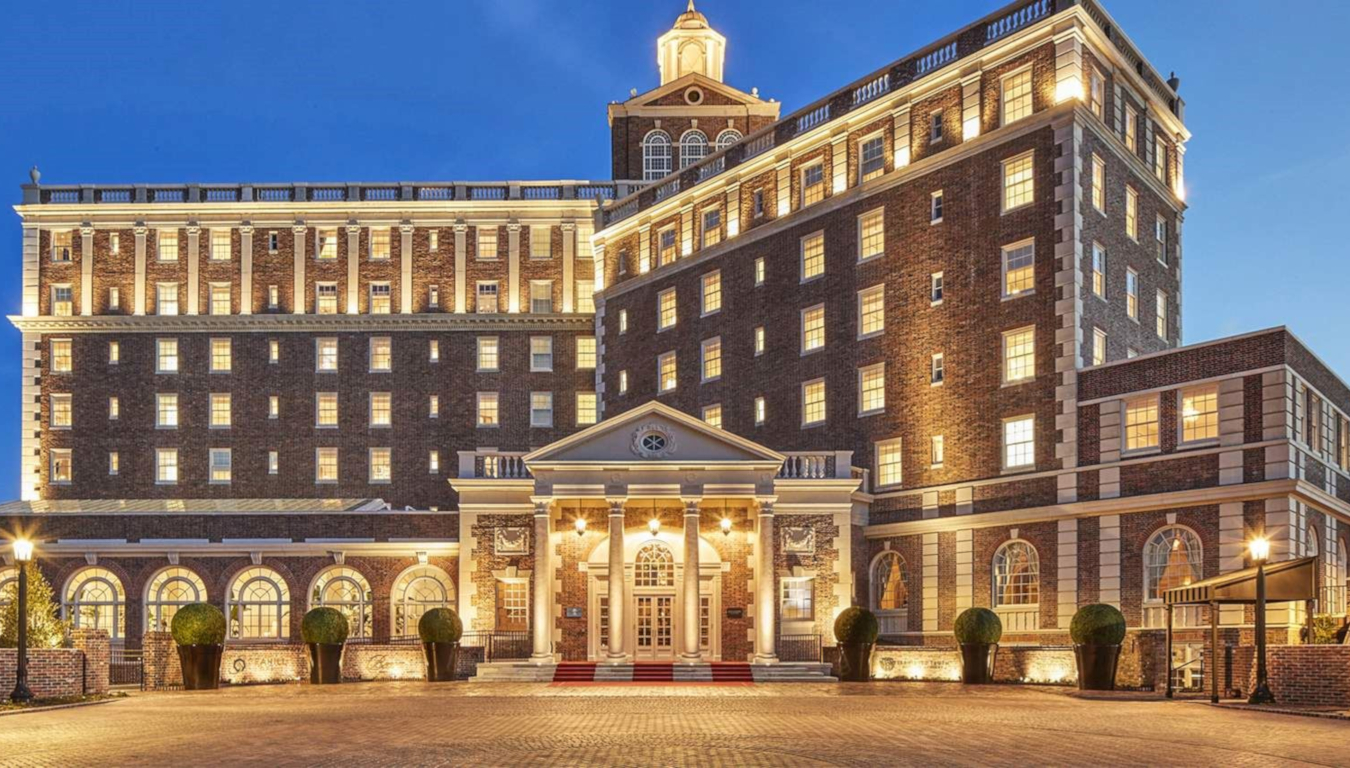 View at dusk of the historic classic brick and white stone six story Cavalier Hotel with arched windows and a pediment and columns at the entrance