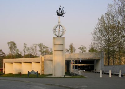 View from the street of the walkway and white concrete louvered building of the Mariners Museum with a giant statue of a compass in front of it