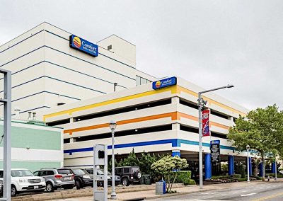 View from the street of the colorful three story parking lot and the ten story Comfort Inn & Suites Virginia Beach with trees and sidewalk in front of it