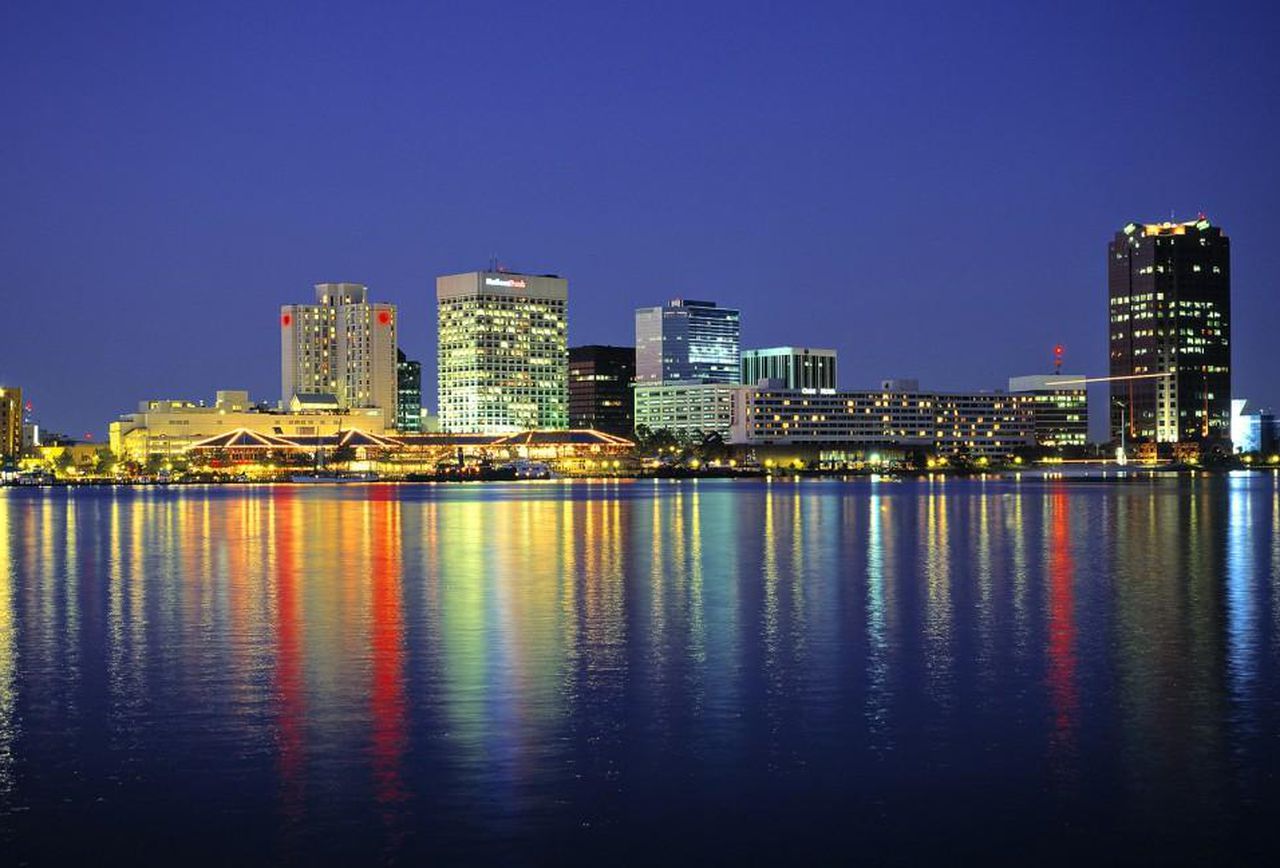 Downtown Norfolk Virginia skyline shown at dusk with colorful lights of the Hampton Roads buildings reflecting on the water
