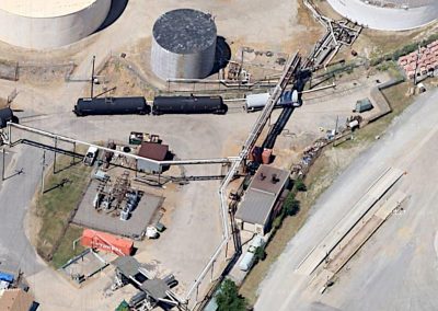 Ariel view of Kinder Morgan Tank Terminals showing long, raised piping runs, silohs, tank style rail cars and sets of pumps on the site with the operations buildong