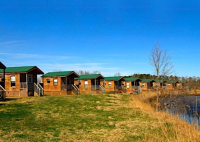 Waterside view of a group of mini log cabins with small front porches at the North Landing RV Park